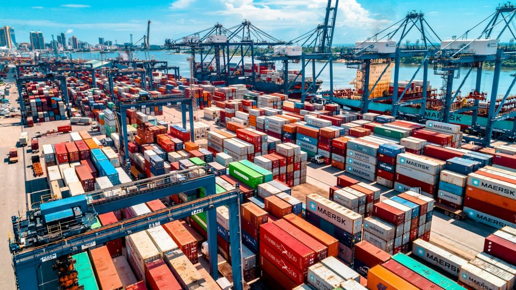 Stacked shipping containers and cranes at a busy port