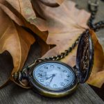 Gold pocket watch lying on dry autumn leaves