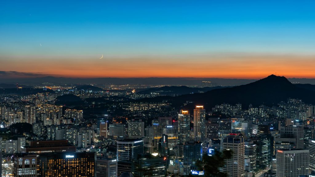 Seoul's illuminated skyline at night under a crescent moon