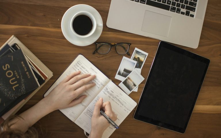 Reporter writing notes in a notebook beside a laptop and coffee