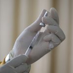 Gloved hands drawing vaccine from a vial into a syringe