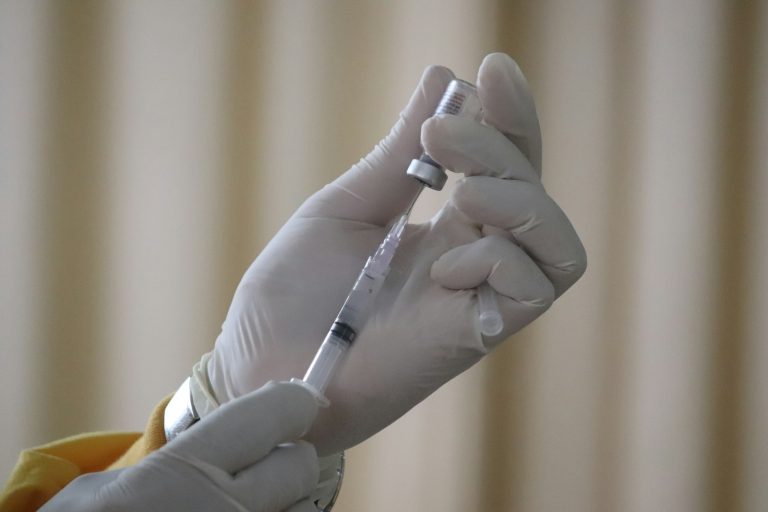 Gloved hands drawing vaccine from a vial into a syringe