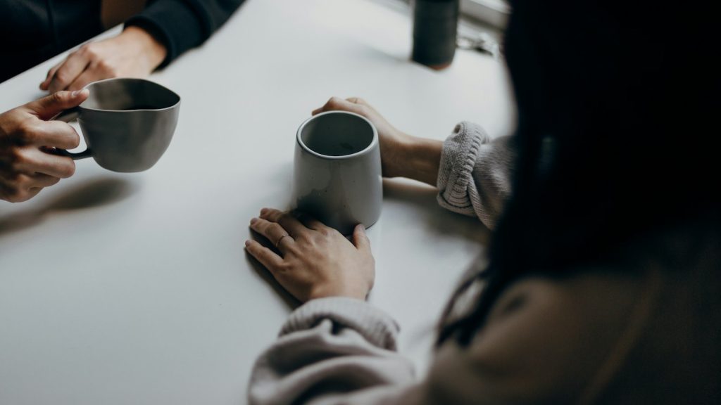 Two people talking over mugs of coffee at a table