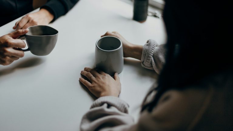 Two people talking over mugs of coffee at a table